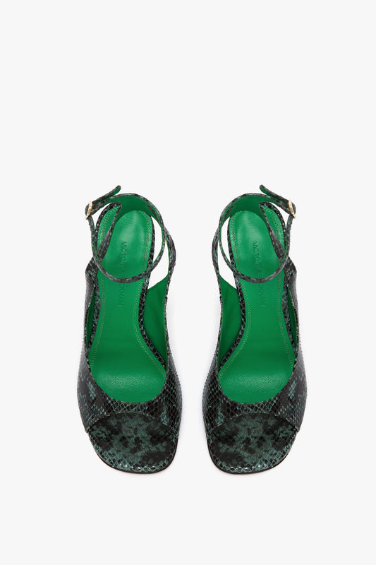 The Victoria Beckham Dawn Sandal in Petrol Green Printed Snakeskin features black and green textured high-heeled sandals with striking green insoles and adjustable snake print ankle straps, displayed elegantly against a white background.