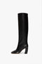 A single black, knee-high boot crafted from luxurious black calf leather, featuring a rounded toe and sturdy 115mm block heel. This tall pull-on Capri Rise Boot 115mm in Black by Victoria Beckham is displayed in a side profile against a plain white background.