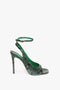 Introducing the Dawn Sandal in Petrol Green Printed Snakeskin: a green snake print high-heel shoe with an elegant ankle strap and buckle, displayed against a plain white background by Victoria Beckham.