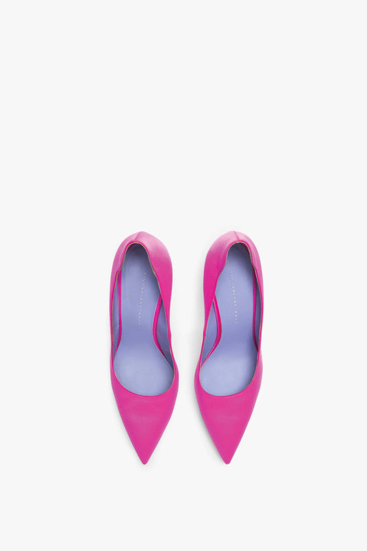 A pair of brightly colored pink pointed-toe high-heeled shoes with light purple insoles, handcrafted in Italy from bright fuchsia satin pump fabric, featuring a sleek 90mm stiletto heel, viewed from above on a white background. The VB 90 Pumps by Victoria Beckham add a bold touch to any outfit.